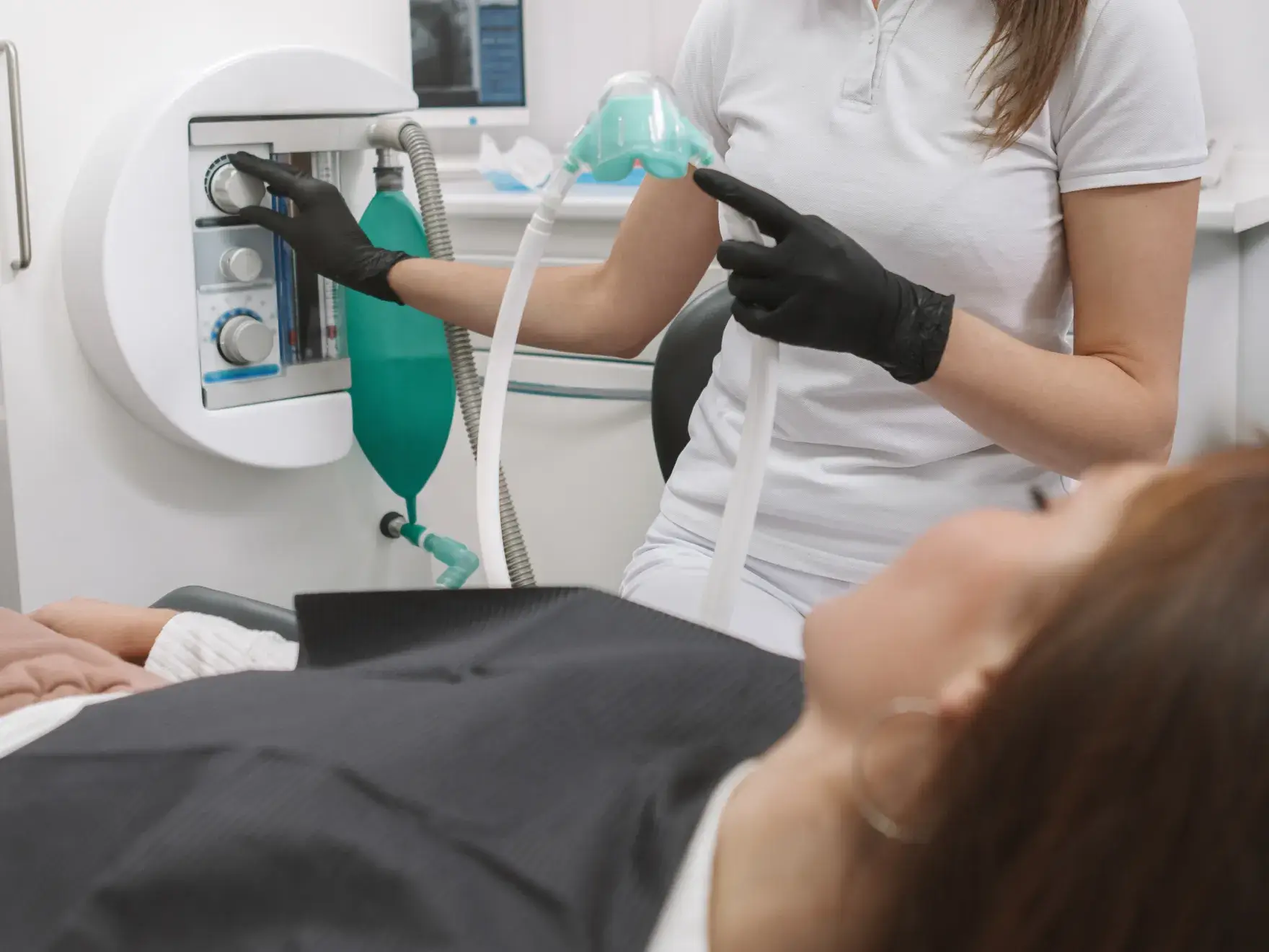 A dentist adjusts equipment while a patient lies on a chair during a dental procedure.