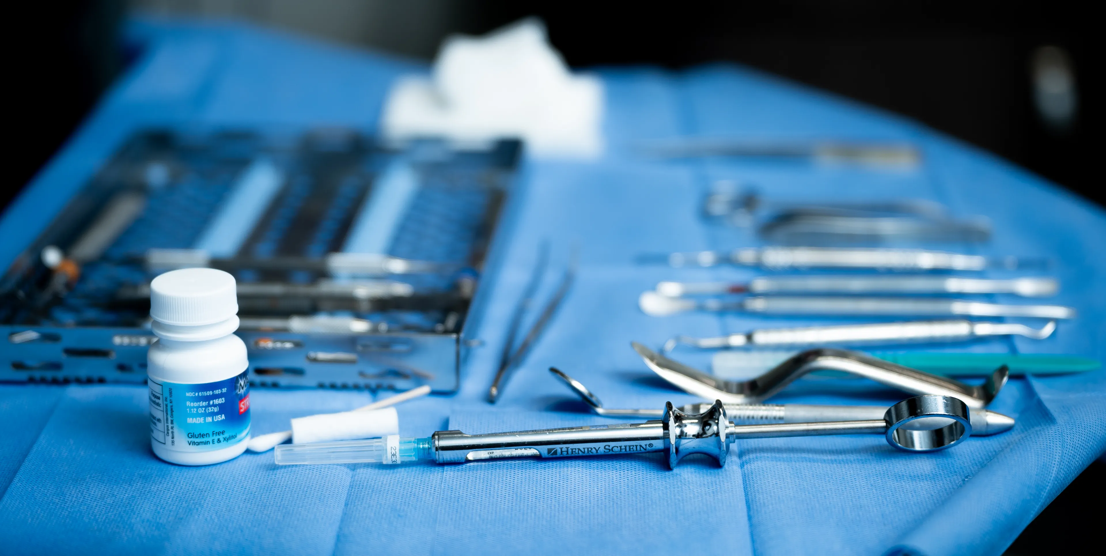 Dental tools and a bottle of medication are arranged on a blue cloth in a dental office.