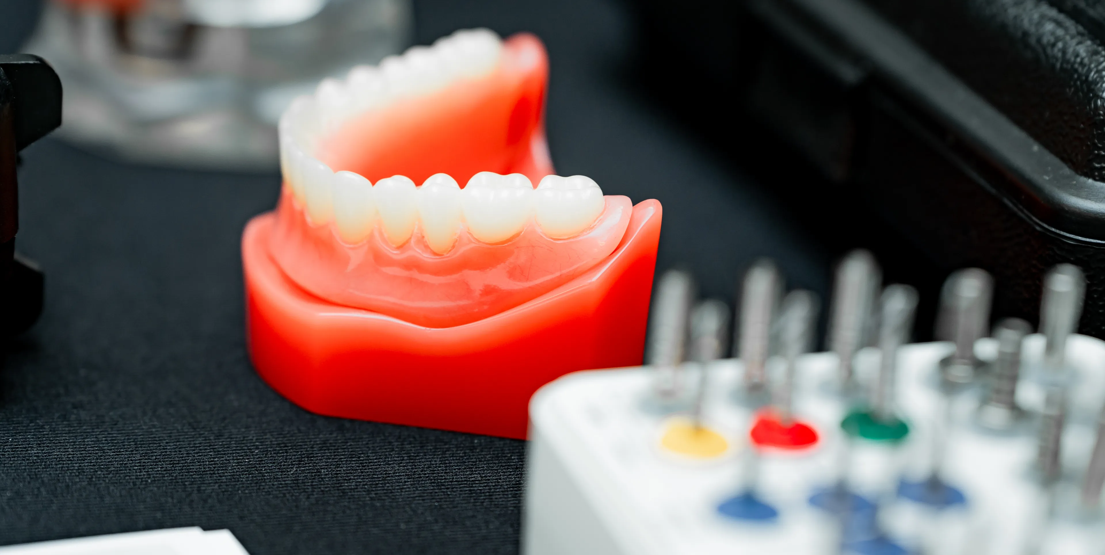 A set of red dental model teeth is displayed on a table next to dental tools.