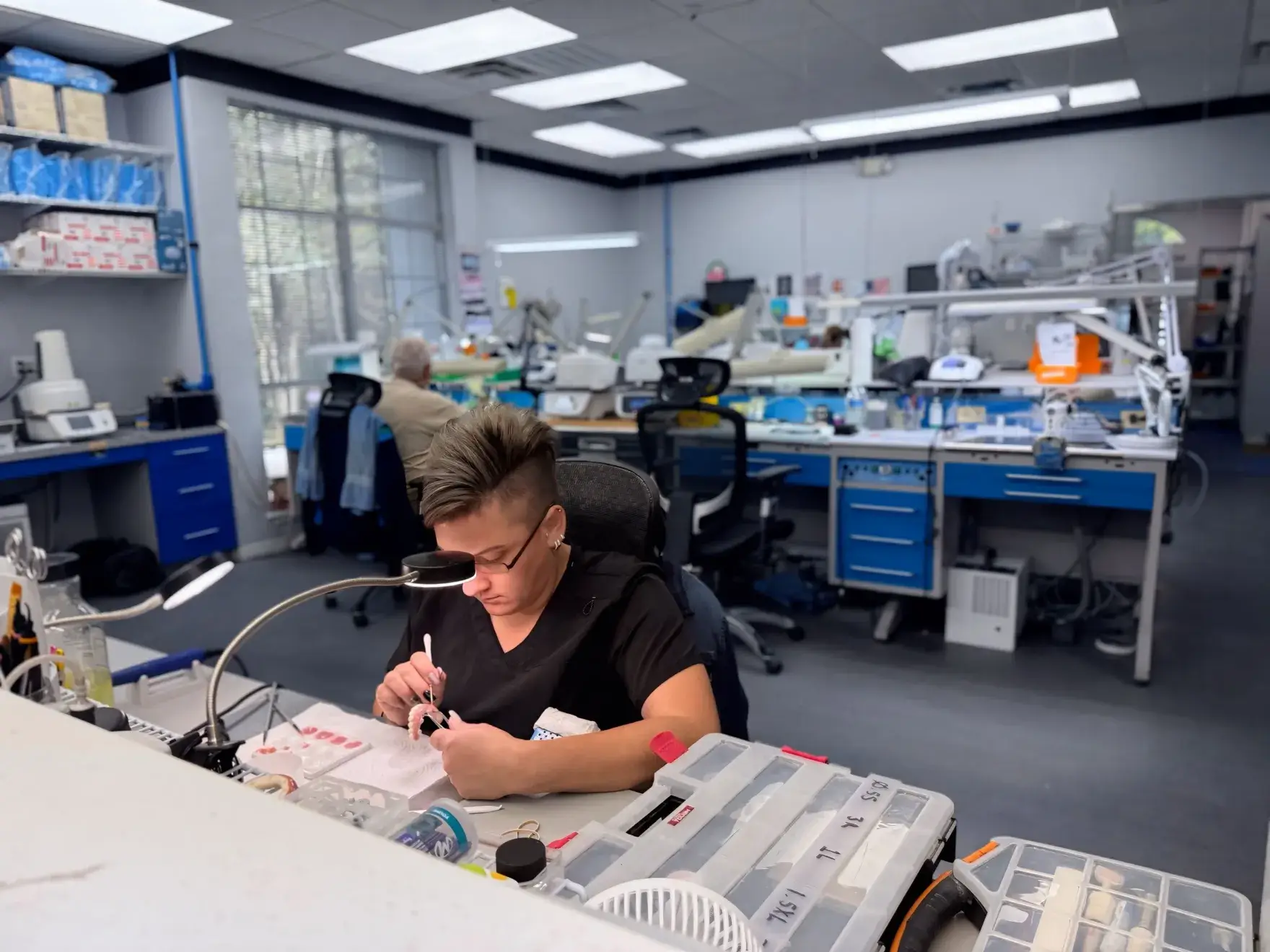 A person works on a dental model in a lab with various dental equipment around.